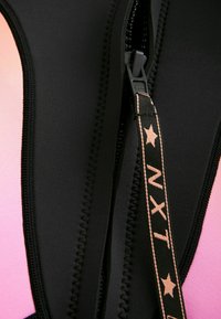 Une combinaison en néoprène noire avec un détail de fermeture éclair. Présente un design en dégradé passant du rose au noir, avec des coutures contrastantes et une languette de tirage à motifs en étoiles.