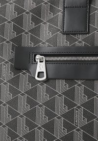 Black textured bag with white geometric pattern. Features a black zipper with silver hardware and a rectangular leather patch.