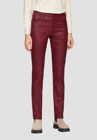 Burgundowe spodnie z faux skóry o slim fit, pięciopunktowym kroju, subtelnym połysku oraz kontrastujących jasnych butach.