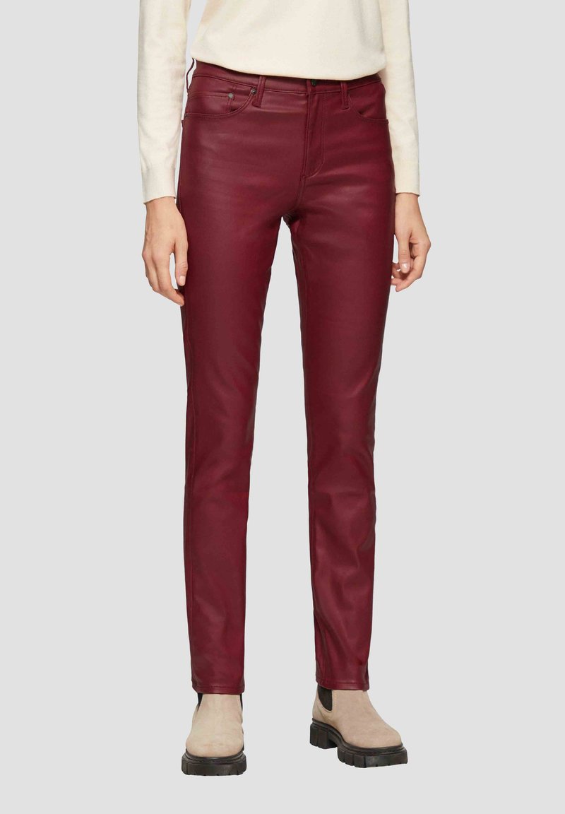 Burgundowe spodnie z faux skóry o slim fit, pięciopunktowym kroju, subtelnym połysku oraz kontrastujących jasnych butach.