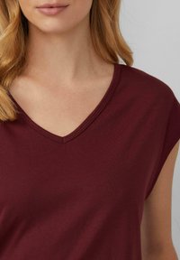 Burgundowa bluzka z dekoltem w serek wykonana z gładkiego, elastycznego materiału, z krótkimi rękawami i dopasowanym krojem, z czystymi szwami wzdłuż dekoltu.