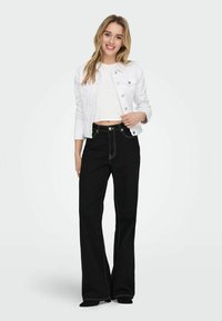 White cropped denim jacket with silver buttons, paired with black wide-legged pants featuring white stitching. Model stands in a neutral background.