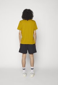 Hořčičná žlutá tílko s krátkým rukávem v kombinaci s černými šortkami. Tkanina vypadá hladce a střih je ležérní a pohodlný.