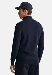 Pull-over en tricot navy avec un col haut, des poignets et un ourlet côtelés, et une texture lisse avec des détails subtils de couture aux épaules.