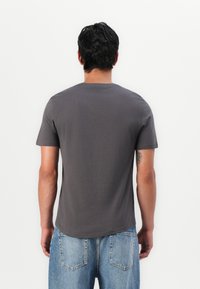 Graues Baumwoll-T-Shirt mit rundem Ausschnitt und kurzen Ärmeln, von hinten angezeigt, kombiniert mit hellblauen Jeans.