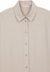 Camicia beige con colletto, realizzata in un tessuto testurizzato. Presenta cinque bottoni sulla parte anteriore e un'etichetta interna.