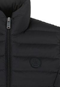Giacca a vento nera con colletto alto, design trapuntato, chiusura con zip e un logo circolare con la scritta "JOTT" sul lato sinistro.