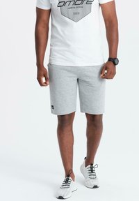 Pantaloni sportivi grigi con una texture melange, abbinati a una maglietta bianca con grafica, e scarpe da ginnastica bianche leggere con dettagli neri.