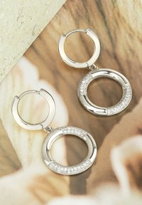 Silver cirkulära hoopörhängen har en polerad yta med ett dekorativt band av klara kristaller på den nedre delen.