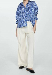 Blue floral-patterned button-up shirt featuring three-quarter sleeves, paired with white wide-leg pants and black slip-on shoes.