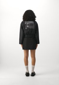 Černé šaty ve stylu bundy s elastickým pasem a dlouhými rukávy. Na zadní straně je velký grafický potisk. Stylizováno s kotníkovými ponožkami a botami.
