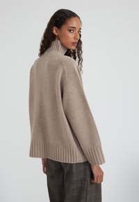 Maglione beige lavorato a maglia con colletto alto, orlo a coste e maniche ampie, caratterizzato da una vestibilità comoda e una texture morbida.