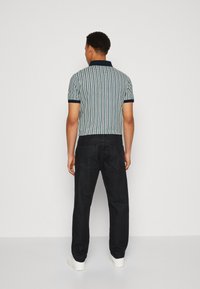 Polo-shirt à manches courtes en marine avec un motif texturé, associé à un pantalon en denim foncé et des baskets blanches, doté d'un col classique.