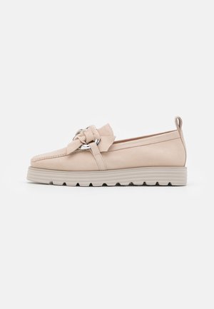 Mocassin beige en cuir à enfiler avec semelle épaisse à rainures, grand nœud décoratif et anneau métallique sur le dessus, vu de côté.