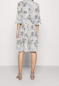 Kukkakuosiset mekko vaaleassa kermassa, jossa tummansiniset ja vaaleansiniset kuviot, lyhyet kellot huput ja liehuva helma. Yhdistetty vaaleanbeigeihin korkokenkiin.