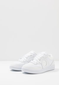 Vita sportskor i slätt lädermaterial, med en rund logopatch, perforerade detaljer och en strukturerad gummisula.