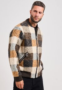 Giacca bomber testurizzata con motivo a quadri in tonalità di marrone, beige e blu. Caratterizzata da una chiusura zip frontale e polsini a costine, con tasche laterali.
