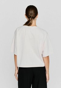 Lichtroze t-shirt met korte mouwen, een ontspannen pasvorm, ronde halslijn en een soepele textuur. Draagt met zwarte broek, wat een eenvoudig ontwerp laat zien.