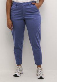 Pantaloni su misura di un azzurro chiaro, dal tessuto morbido, con vita media e tasche laterali, abbinati a sneakers bianche e grigie.