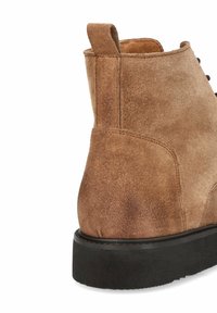 Brązowy zamszowy botek za kostkę z solidną czarną gumową podeszwą, z teksturowanym wykończeniem i pętelką z tyłu ułatwiającą zakładanie.
