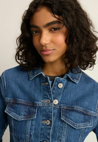 Denim jacket in medium wash blue with silver hardware, two chest pockets, button-up front, and classic collar design.