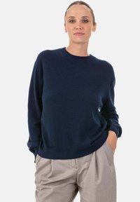 Pull tricoté bleu marine avec col rond, manches longues et poignets et ourlet côtelés, associé à un pantalon taille haute beige clair.