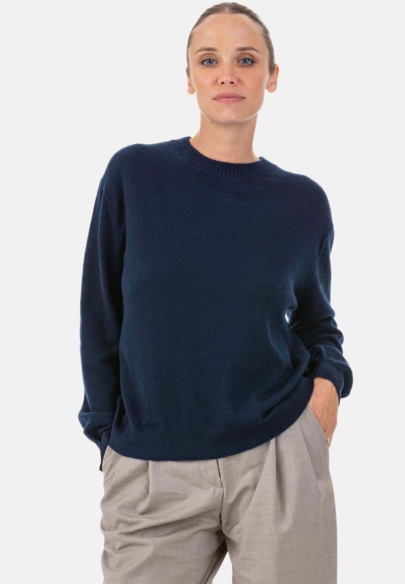 Pull tricoté bleu marine avec col rond, manches longues et poignets et ourlet côtelés, associé à un pantalon taille haute beige clair.