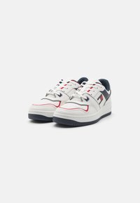 Zapatillas blancas con un acabado de cuero liso, acentos en rojo y marino, puntera perforada, cuello acolchado y suela de goma.