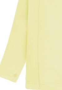 Λεπτομέρεια μανικιού και πλευρικού φερμουάρ σε ανοιχτό κίτρινο fleece μπουφάν, που δείχνει υφή υφάσματος και ραφές κοντά στον καρπό και το τελείωμα.