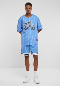 Tricou de baseball bleu deschis cu literă neagră și dungi albe, asociat cu pantaloni scurți bleu asortați, cu detalii negre și borduri albe. Adidași albi.