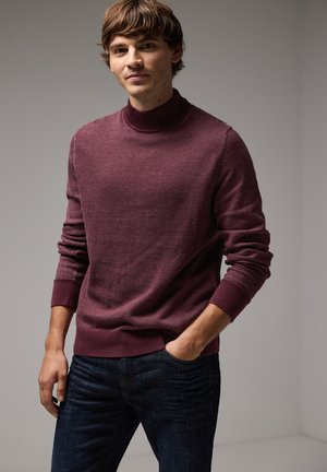 Bordeaux coltrui van een zachte stof, met geribbelde boorden en zoom, gecombineerd met donkerblauwe jeans voor een casual uitstraling.