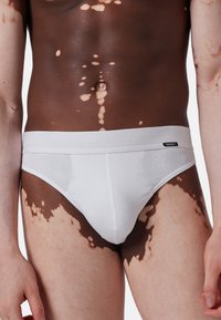 Mutande bianche in cotone con una superficie liscia e un elastico in vita, realizzate su una tonalità della pelle con diverse sfumature e motivi.