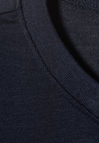 Navy cotton sweater close-up, featuring a ribbed round neckline and smooth texture, with visible stitching on the collar and body.