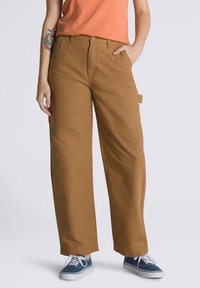 Tan wide-leg cargo pants made of cotton, featuring side pockets, a button closure, and cuffed hems, paired with blue canvas sneakers.