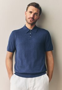 Marineblaue, gestrickte Poloshirt mit kurzen Ärmeln, Dreiknopfleiste, geripptem Saum und Kragen, kombiniert mit hellen Hosen.