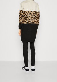 Gehaakt sweater in beige, zwart en tan luipaardprint. Lange mouwen, relaxte pasvorm en iets langere achterkant. Gecombineerd met zwarte legging en sneakers.