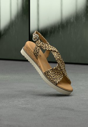 Leopard-print sandal with cross straps, cork midsole, and a white rubber zigzag sole. Silver buckle accent near the ankle.