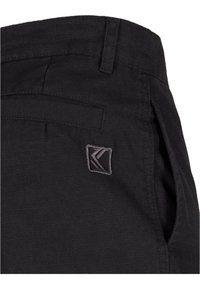 Sorte bomullsblandingsbukser med teksturert overflate, som har en skrå lomme og en liten brodert logo i grått på midjebåndet.