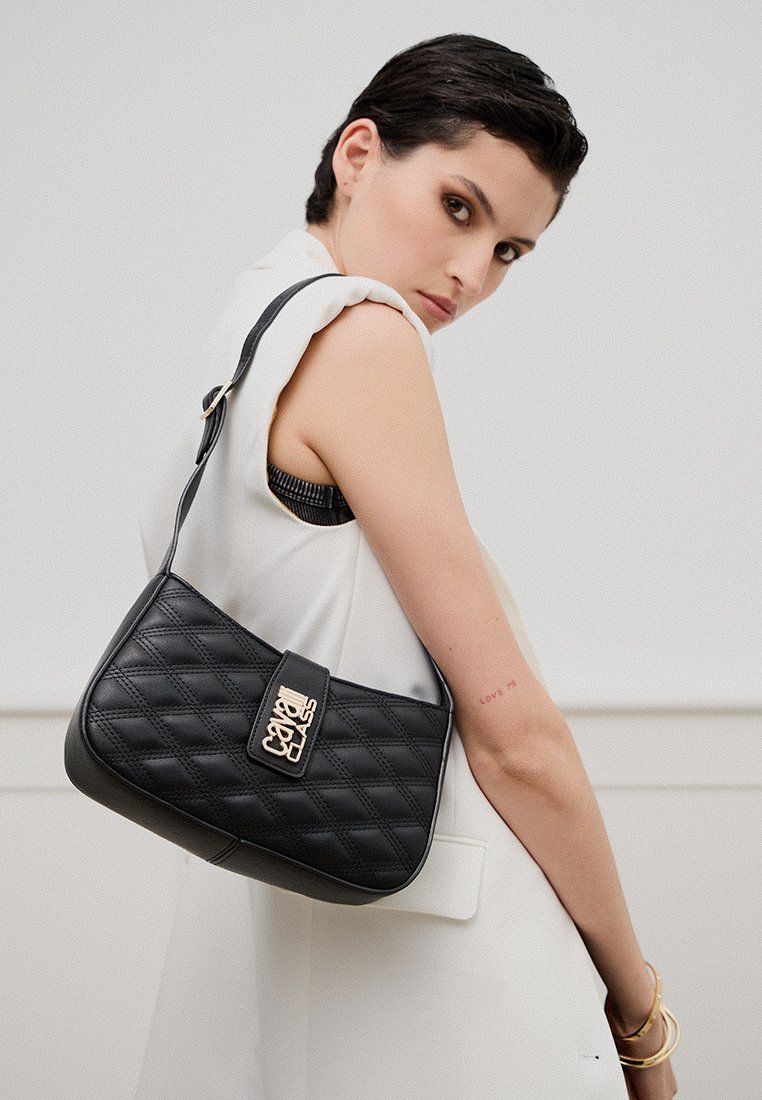 Borsa a tracolla in pelle nera trapuntata con chiusura in tonalità oro e tracolla regolabile; presenta una texture liscia e una forma rettangolare.