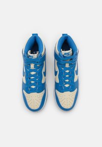 Höga sneakers med en blå läderöverdel och beige detaljer, perforerad tåbox och blå snören. Nike-logga på tungan och sidorna.
