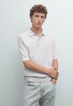 Light gray knit polo shirt with a classic collar, short sleeves, three buttons, and ribbed cuffs, paired with light denim jeans.