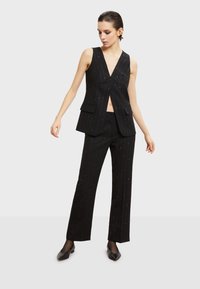 Czarna kamizelka w paski z głębokim dekoltem w kształcie litery V i rozcięciem z przodu, połączona z dopasowanymi spodniami. Obie części mają dopasowany krój i subtelny połysk.