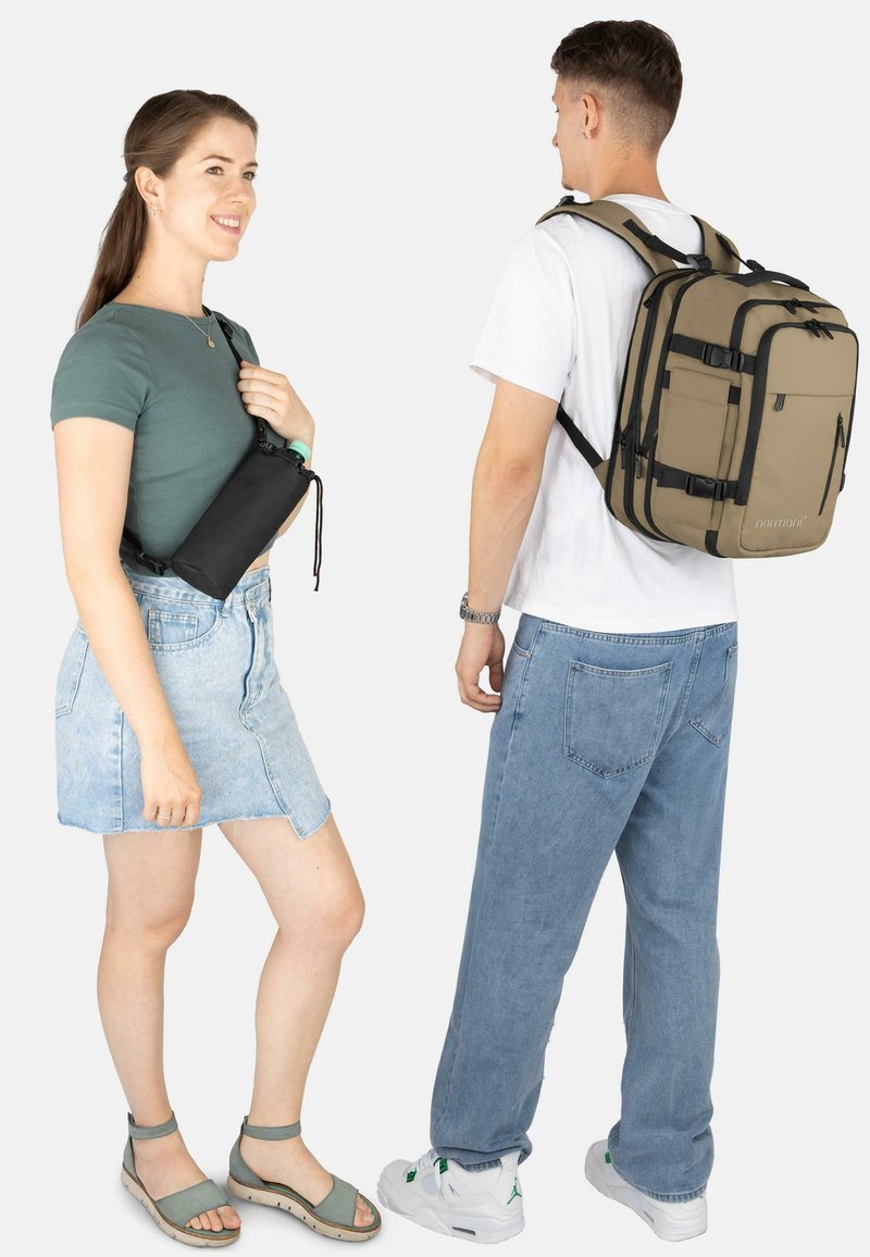 Schwarze, kompakte Umhängetasche, getragen von einer Person mit grünem Oberteil und Jeansrock. Ein beiger Rucksack mit mehreren Taschen bei einer anderen Person in hellen Jeans.