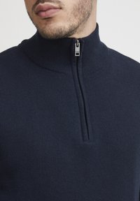 Mörkblå halvsidig zip-tröja i stickad tyg med ribbad krage och metalldragkedja, med en mjuk yta och figurnära design.