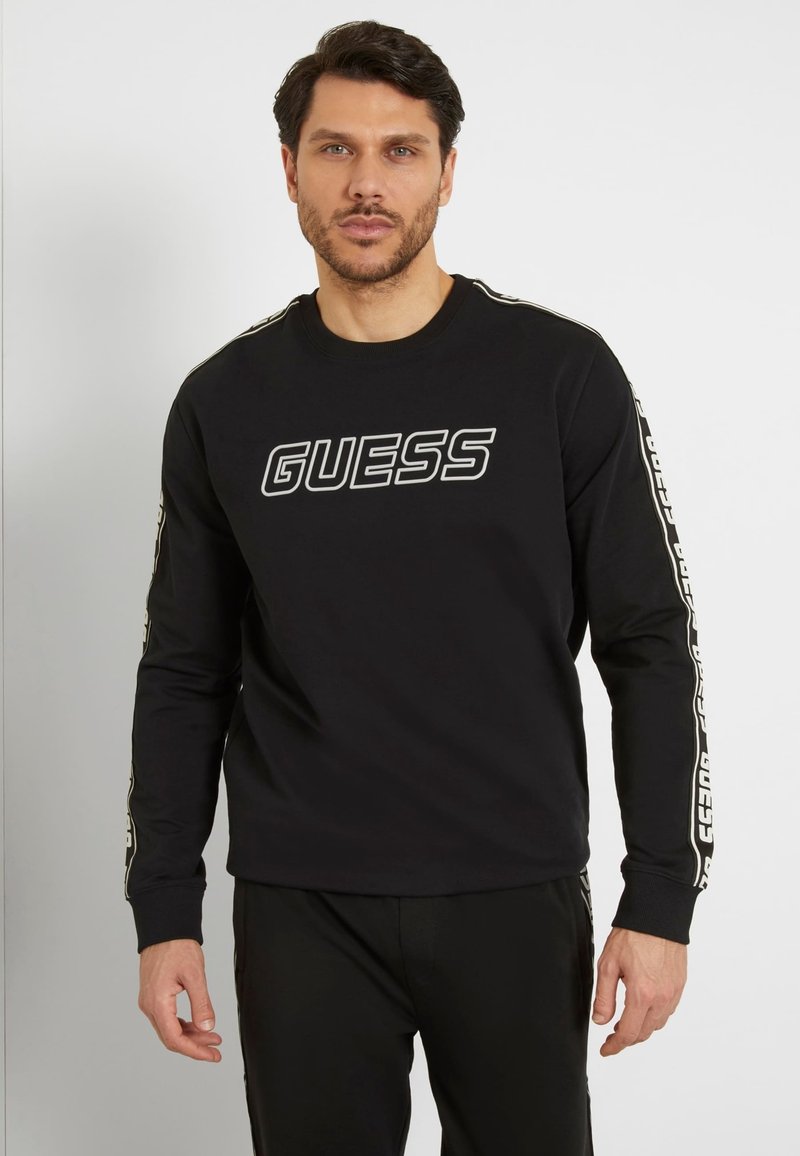 Felpa nera a maniche lunghe con logo "GUESS" stampato sul davanti, caratterizzata da dettagli decorati lungo le maniche e un colletto tondo.