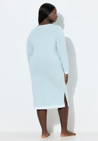 Lyseblå natkjole med lange ærmer, lige snit og hvid bølget kant forneden, med sidesplitter for nem bevægelse.