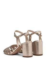 Sandalias de tacón metálico dorado con tiras entrelazadas y tacón bloque. Diseño de punta abierta y textura suave, que muestra una silueta moderna.