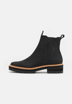 Zwarte leren Chelsea-boot met elastische zijpanelen, beige stiksel, robuuste zool en lussen bij de enkelkraag.
