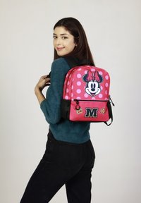 Mochila rosa con puntos de Polka y un gráfico de Minnie Mouse. Incluye detalles en negro, un bolsillo frontal con cremallera y detalles decorativos en el herraje.