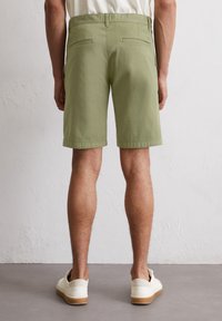 Light green cotton shorts with a straight cut, two back pockets, and a clean hem, paired with white sneakers on a gray surface.